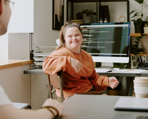 Wide shot of female programmer with down syndrome sitting on chair and looking at her male coworker